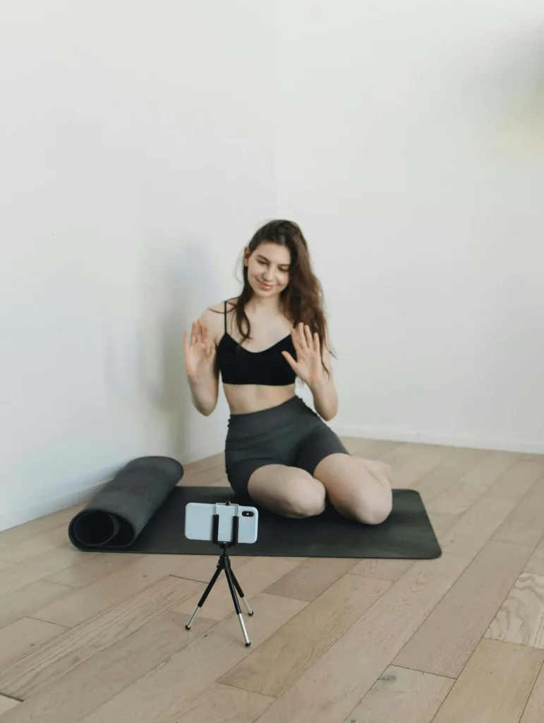 A girl capturing her morning yoga activity throgh her smartphone fixed with tripod holding it above the floor.